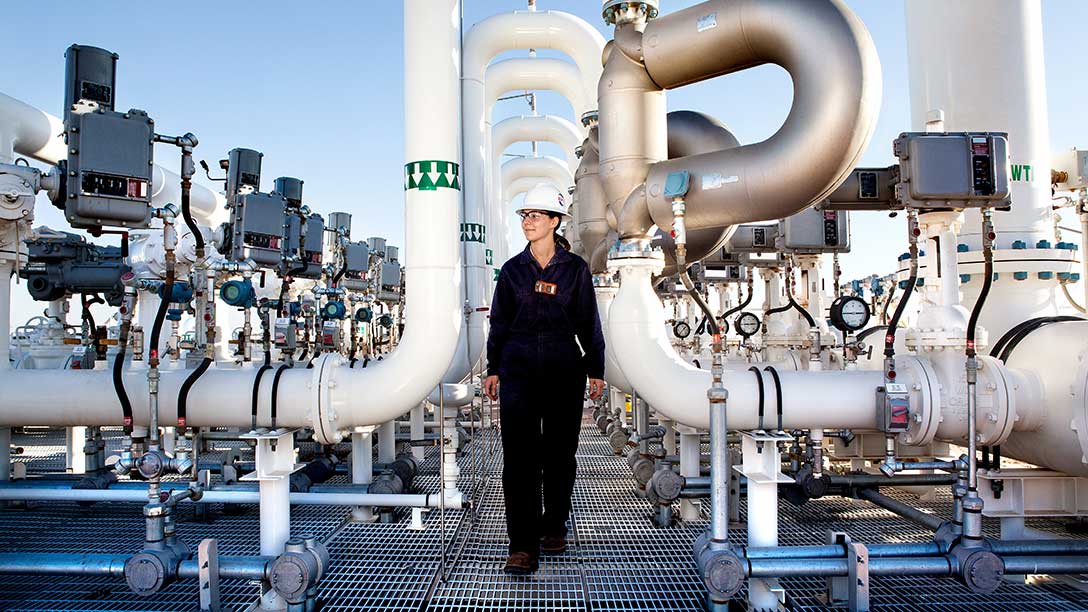 Oxy female employee walking through pipes in Permian